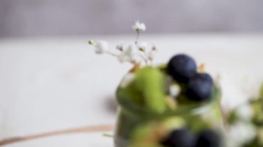 Kivili Chia pudingi, yabanmersini ve hindistan cevizi dilimleri, beyaz bir masada cam kavanozlarda üç porsiyon..