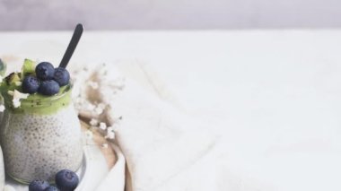 Kivili Chia pudingi, yabanmersini ve hindistan cevizi dilimleri, beyaz bir masada cam kavanozlarda üç porsiyon..