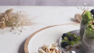 Kivili Chia pudingi, yabanmersini ve hindistan cevizi dilimleri, beyaz bir masada cam kavanozlarda üç porsiyon..