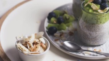 Kivili Chia pudingi, yabanmersini ve hindistan cevizi dilimleri, beyaz bir masada cam kavanozlarda üç porsiyon..