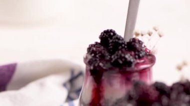 Böğürtlenli Chia pudingi, beyaz bir masada cam kavanozlarda üç porsiyon.