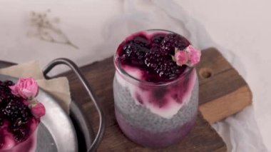 Böğürtlenli Chia pudingi, beyaz bir masada cam kavanozlarda üç porsiyon.