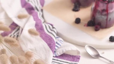 Böğürtlenli Chia pudingi, beyaz bir masada cam kavanozlarda üç porsiyon.