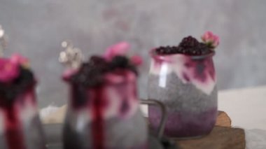 Böğürtlenli Chia pudingi, beyaz bir masada cam kavanozlarda üç porsiyon.