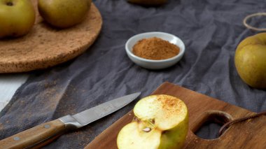 Tarçınla kaplanmış altın elma kamışı, arka planda yarısı kesilmiş bir elmayla kırsal bir tahta kesme tahtasının üzerinde sunuluyor. Sahne, yumuşak odak ve toprak tonları ile, lezzetli bir ev yemeği hazırlama samimi, sonbahar hissi uyandırır