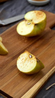 Tarçınla kaplanmış altın elma kamışı, arka planda yarısı kesilmiş bir elmayla kırsal bir tahta kesme tahtasının üzerinde sunuluyor. Sahne, yumuşak odak ve toprak tonları ile, lezzetli bir ev yemeği hazırlama samimi, sonbahar hissi uyandırır