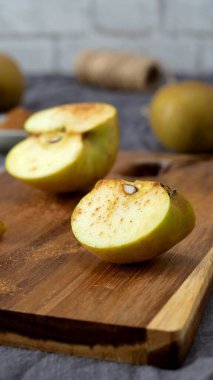 Tarçınla kaplanmış altın elma kamışı, arka planda yarısı kesilmiş bir elmayla kırsal bir tahta kesme tahtasının üzerinde sunuluyor. Sahne, yumuşak odak ve toprak tonları ile, lezzetli bir ev yemeği hazırlama samimi, sonbahar hissi uyandırır