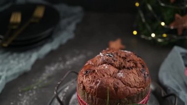 Geleneksel İtalyan Panettone keki, desenli bir kolla sarılmış ve kırmızı kadife kurdele ve biberiye filizi ile bağlanmış metal servis tabakları üzerine kuruludur..