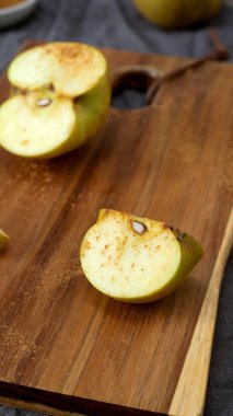 Tarçınla kaplanmış altın elma kamışı, arka planda yarısı kesilmiş bir elmayla kırsal bir tahta kesme tahtasının üzerinde sunuluyor. Sahne, yumuşak odak ve toprak tonları ile, lezzetli bir ev yemeği hazırlama samimi, sonbahar hissi uyandırır