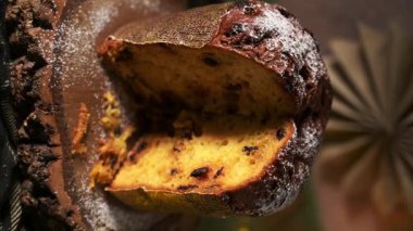 Geleneksel İtalyan panettonunun dramatik, dikey bir yakın çekimi, kısmen nemli, altın iç ve görünür meyveyi göstermek için kesilmiş, pudra şekeriyle kaplı.