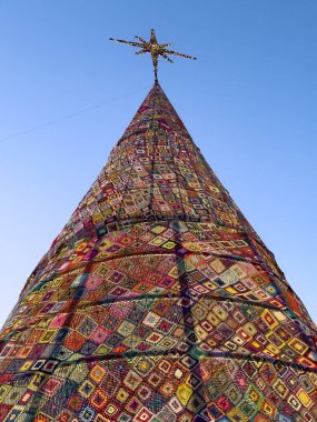 Aşırı düşük açılı bir perspektif, Portekiz 'in Ovar kentindeki Cortegaca Sahili' ndeki devasa, aydınlık Noel ağacının yüzeyini kaplayan örgü örme karelerinin karmaşık ve renkli yamasını vurguluyor. Tekstil deseni...