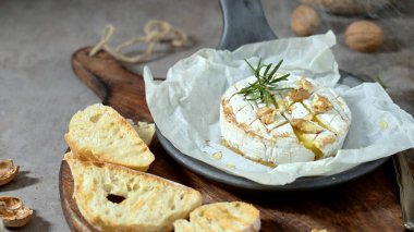 Bir tekerlek erimiş camembert peyniri üzerine kıtır ceviz ve parşömen kağıdında taze biberiye ile kaplıdır. Kırsal aperatifler ahşap bir tahtanın üzerinde yumuşak ışık altında kabuklu ekmekle servis edilir..