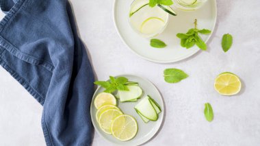 İçi doldurulmuş su dolu parlak ve temiz bir masa manzarası. Dilimlenmiş limon, salatalık kurdeleleri ve parlak nane filizleri mavi keten peçeteyle birlikte tabaklara dizilmiştir..