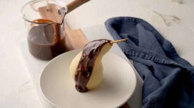 Minimalist bir gurme tatlı, yumuşak haşlanmış armut, parlak, siyah çikolata sosuyla süslenmiş. Parlak, yüksek tuşlu ayar dokuları vurgulamak için yumuşak doğal ışık kullanır..