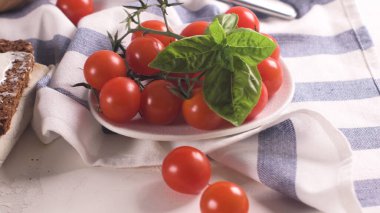 Parlak, yüksek açılı, olgun kırmızı kiraz domatesleri ve yeşil fesleğen renginde kırsal bir keten kumaş. Yumuşak doğal ışık yumuşak dokuları ve canlı renkleri vurgular.