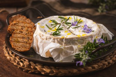 Yumuşak bir peynirin üzerine taze biberiye filizi ve zeytinyağı serpilmiştir. Sıcak, karamsar ışıklandırma kremalı dokuya ve gevrek tahıllı ekmek dilimlerine vurgu yapıyor..
