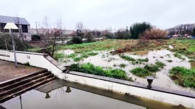 Ovar, Portekiz - 10 Şubat 2026: Yoğun bir yağmur döneminden sonra çamurlu su altında kalmış bir park alanı ve yürüyüş yolunu gösteren kentsel manzara.
