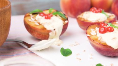 Kremalı Yunan yoğurdu, kızarmış yulaf ve tart kırmızısı frenk üzümlü kavrulmuş şeftali. Bu parlak, yazlık yemek çekimi yumuşak doğal aydınlatma ve sağlıklı, kırsal bir estetik içeriyor..