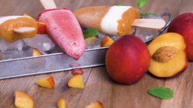 Metal bir tepside buz yatağında dinlenen canlı meyve şekerlerinin olduğu ferahlatıcı bir yaz sahnesi. Bileşim, köy ahşap yüzeyinde dilimlenmiş nektarinler ve nane yapraklarını içeriyor..