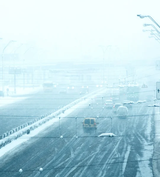 Route d'hiver enneigée avec des voitures conduisant sur la chaussée dans la tempête de neige — Photo