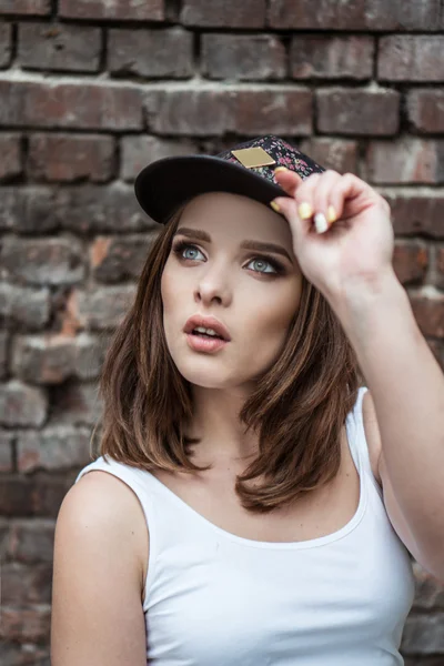 Bonita mujer en la pared de ladrillo con sombrero deportivo —  Fotos de Stock