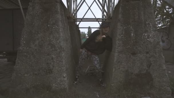 Активная молодая женщина танцует между бетонными колоннами в замедленной съемке . — стоковое видео