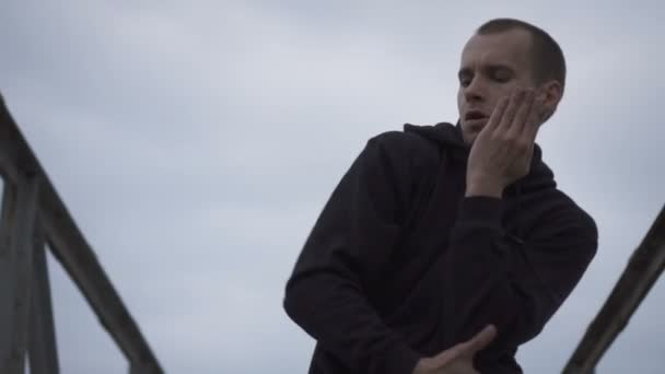 Jeune homme actif dansant sur le pont au ralenti, ciel derrière lui . — Video