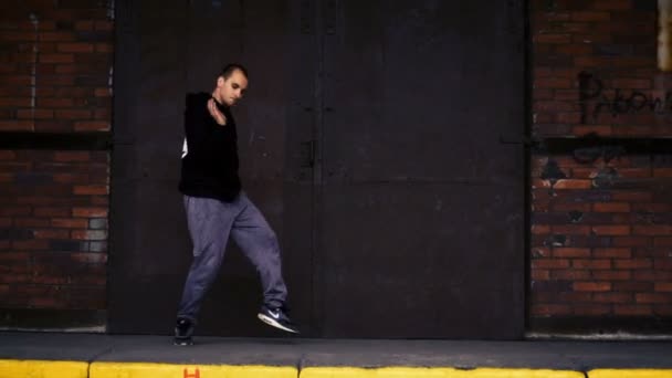 Aktiver junger Mann tanzt auf einer schwarzen Metalltür und Backsteinmauer. — Stockvideo