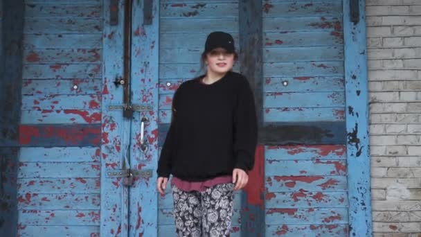 Actieve jonge vrouw dansen op een oude blauwe deur en bakstenen muur achtergrond in slow motion. — Stockvideo