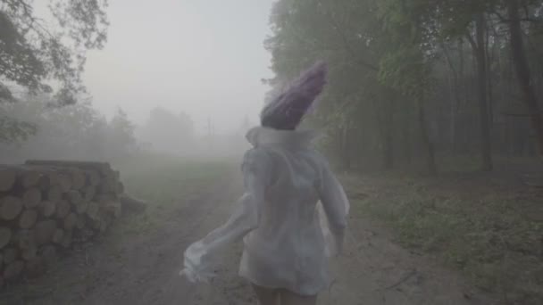 Vista posterior de la hermosa mujer en el pelo púrpura y camisa blanca corriendo en el bosque - escena de suspenso. Video de belleza sensual entre árboles en cámara lenta, niebla y bosque oscuro . — Vídeos de Stock