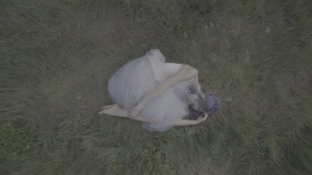 Hermosa mujer en vestido blanco y pelo morado acostado en el suelo en el bosque - escena de cuento de hadas. Video de la belleza despertando en la hierba verde en cámara lenta . — Vídeos de Stock