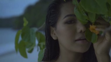 Asyalı güzel kadın kroşe bikini plaj portre. Ağır çekimde ağaçtan çiçek kokulu plajda seksi kız video.