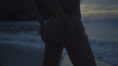 Sahilde tığ işi bikinili güzel kadının yakın çekimi. Sahilde seksi kız Video, yavaş hareket gün batımında görmek ve gökyüzü arka plan ile alt ellerini hareket.