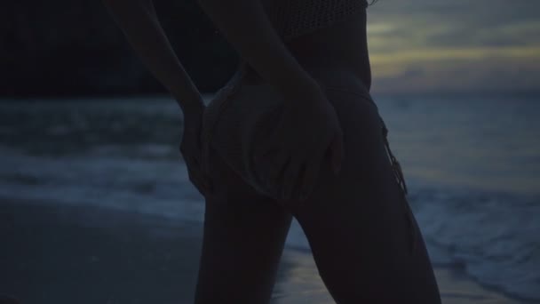 在海滩上穿着钩针比基尼的漂亮女人的特写镜头。性感的女孩在海滩上的视频，移动她的手在底部与看到和天空背景在日落在慢动作. — 图库视频影像