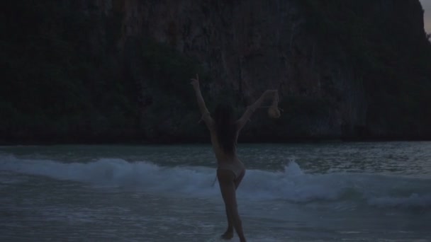 亚洲美丽的女人在钩针比基尼在海滩上跳舞。性感的女孩在沙滩上跳舞的视频与胸罩在她的手中 - 慢动作. — 图库视频影像