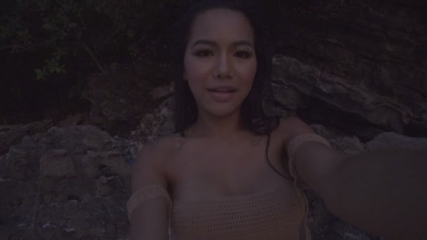 Mujer hermosa y feliz asiática en la playa. Video de la chica sonriente sexy tomando selfie por las rocas en la playa en cámara lenta . — Vídeos de Stock