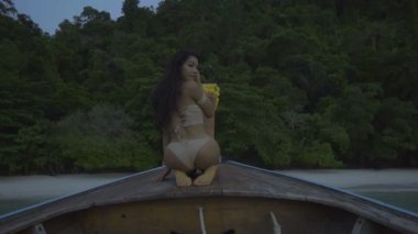Teknede tığ işi bikini Asya güzel şehvetli kadın. Video seksi kız bir yay üzerinde oturan ve kameraya bakarak - yavaş çekimde geri görünümü.