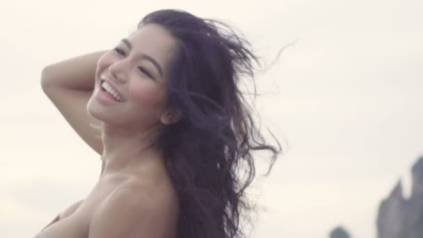 かぎ針編みのビキニでのアジアの美しい幸せな女。風が彼女の髪と笑顔とスローモーションでカメラに探しているセクシーな女の子のビデオ. — ストック動画