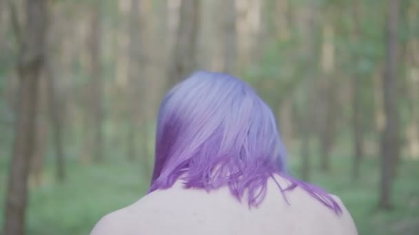 Zbliżenie na twarz ładna kobieta, potrząsając jej fioletowe włosy i patrząc w kamerę. Na białym tle w lesie, w zwolnionym tempie. — Wideo stockowe