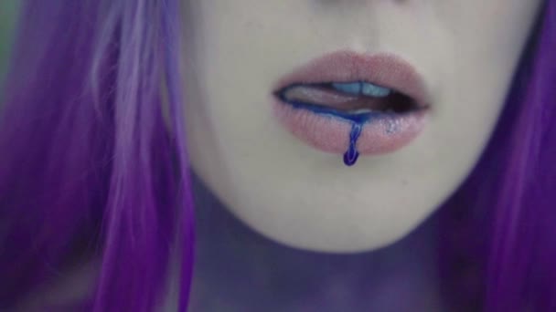 Nahaufnahme einer hübschen Frau mit lila Haaren und blauer Farbe auf den Lippen, die nach unten fällt. Blauer Tropfen tropft von der Unterlippe. — Stockvideo