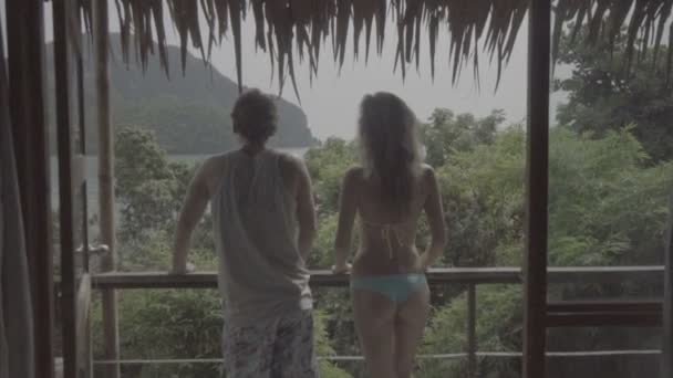 Bella giovane coppia in piedi sulla terrazza dell'appartamento durante le loro vacanze e godendo di una splendida vista sul mare e sulle montagne davanti a loro al rallentatore . — Video Stock