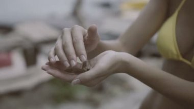 Sarı bikinili genç bir kadın elinde kelebeği tutuyor ve yakın plan yapmaya çalışıyor..