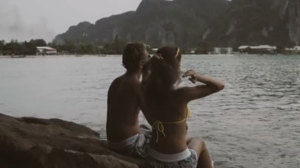 예쁜 젊은 행복한 부부는 앉아서 그들 앞에 아름다운 전망과 함께 휴가 기간 동안 바위에 이야기. — 비디오