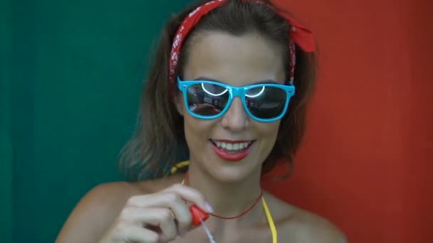 Jolie jeune femme portant un bikini et des lunettes de soleil faisant des bulles de savon isolé sur un mur coloré . — Video