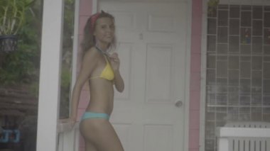 Bikini giyen güzel genç kadın gülümseyerek ve pembe evin terasında poz.