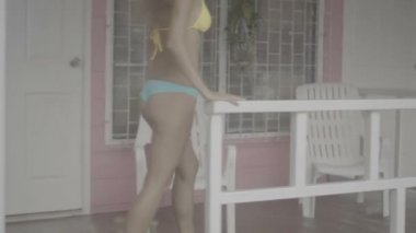 Gülümseyen genç ve güzel kadın giyen bikini ve pembe evde terasta yürüme.