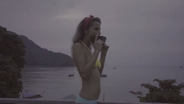 Glad ung kvinna klädd i bikini äta vattenmelon på taket med vacker utsikt bakom. — Stockvideo