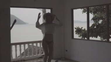 Güzel deniz manzara arka plan üzerinde terk edilmiş bir binada beyaz gömlek, bikini ve şapka dansı giyen boho tarzı moda yaz gününde Pretty doğal görünümlü kadın.