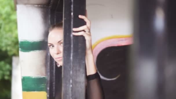 Hermosa mujer rubia con un traje de baño elegante negro y pendientes mirando a través de la ventana en el edificio abandonado sobre paredes con fondo de pinturas . — Vídeos de Stock