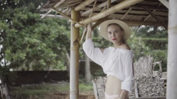 Jolie femme naturellement en mode boho portant une chemise blanche, un bikini et un chapeau par une belle journée d'été - vidéo au ralenti . — Video